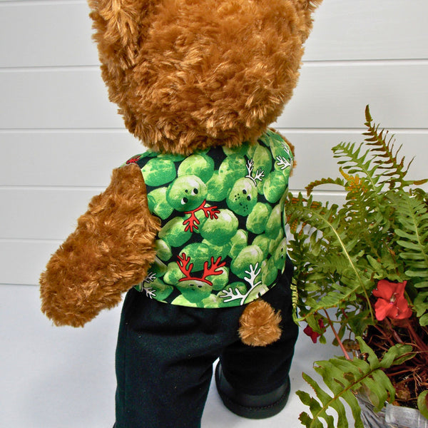 Build a bear teddy bear wearing a green patterned waistcoat, black trousers and black shoes. The teddy bear is standing in front of a white background with a green fern plant to the right. The teddy bear waistcoat and teddy bear pants were made from sewing patterns by Best Dressed Bears.