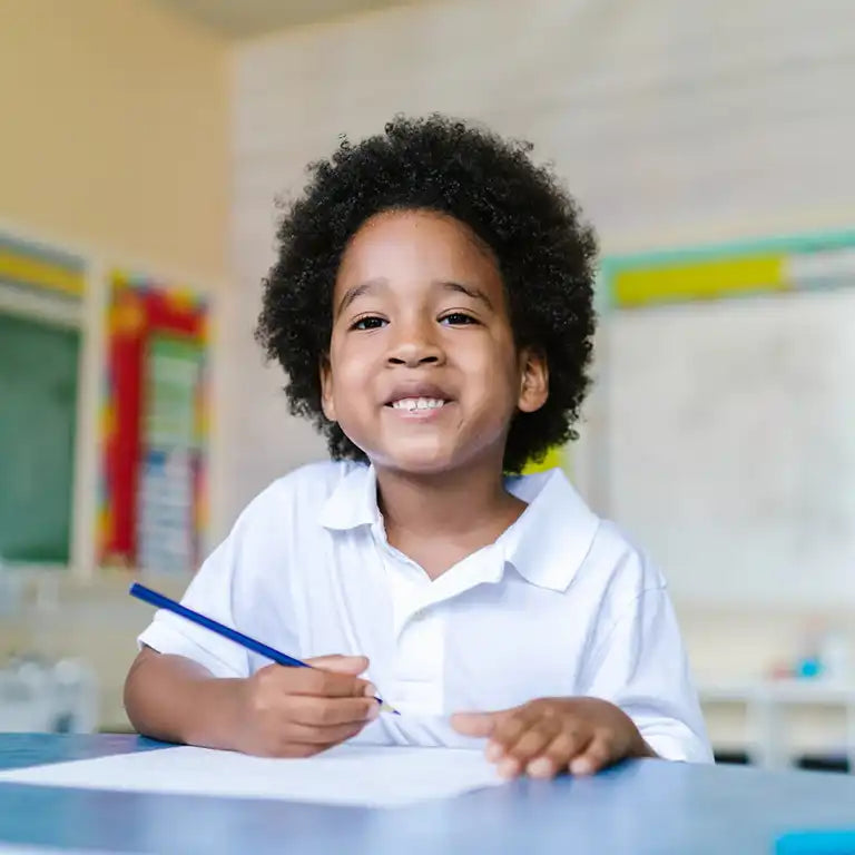 Child sitting at a school desk holding a pencil & wearing a white polo shirt