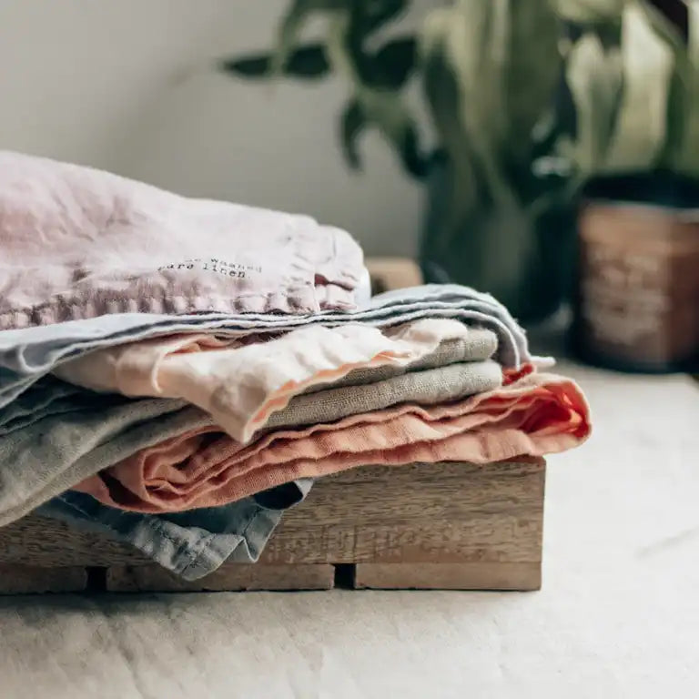 Pile of fabric sitting on a wooden block with a plant in the background