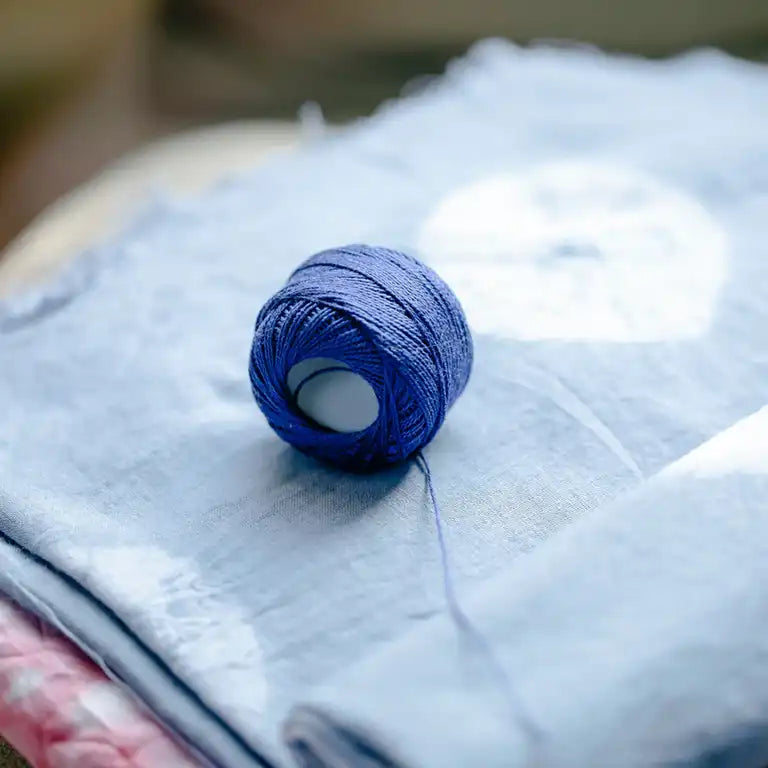 Pile of blue and pink fabric with a reel of thread on top. 