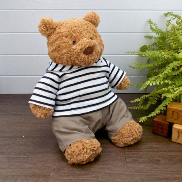 Jellycat Bartholomew teddy bear wearing a black & white striped hoodie and brown trousers sitting next to a potted plant and wooden blocks.