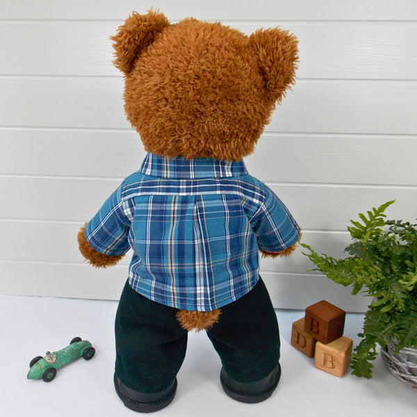 A brown coloured teddy bear wearing a blue checked shirt and black trousers. The teddy bear is standing in front of a white background. The teddy bear shirt and teddy bear trousers have been made from sewing patterns by Best Dressed Bears.