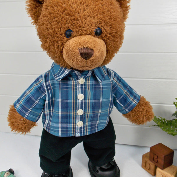 A brown coloured teddy bear wearing a blue checked shirt and black trousers. The teddy bear is standing in front of a white background. The teddy bear shirt and teddy bear trousers have been made from sewing patterns by Best Dressed Bears.