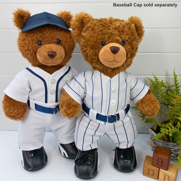 Build a bear teddy bears wearing white and blue baseball outfits with blue belts and black training shoes. One teddy bear is wearing a blue baseball cap. The teddy bears are standing in front of a white background with a green fern plant on the right. There ae 3 wooden bricks with the letters B, D and B depicting the company name of Best Dressed Bears. The teddy bear baseball outfits and the teddy bear baseball cap have been made from sewing patterns by Best Dressed Bears.