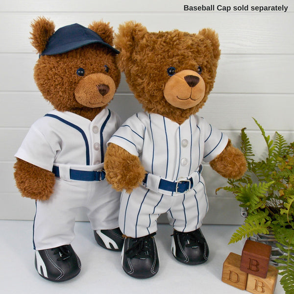 Build a bear teddy bears wearing white and blue baseball outfits with blue belts and black training shoes. One teddy bear is wearing a blue baseball cap. The teddy bears are standing in front of a white background with a green fern plant on the right. There ae 3 wooden bricks with the letters B, D and B depicting the company name of Best Dressed Bears. The teddy bear baseball outfits and the teddy bear baseball cap have been made from sewing patterns by Best Dressed Bears.