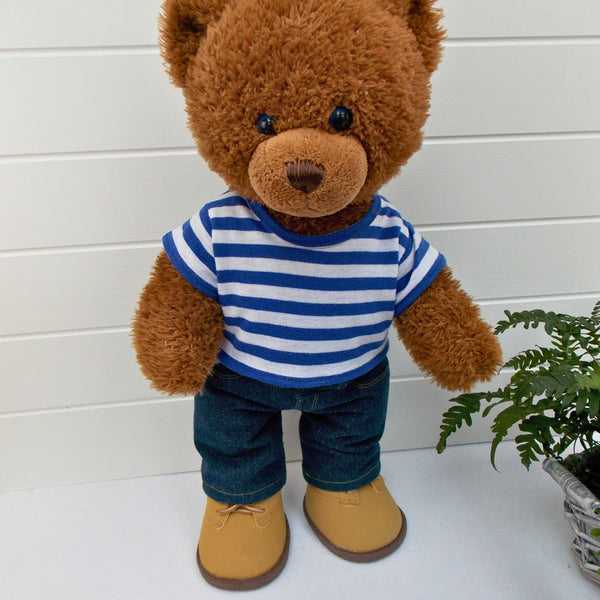 Build a bear teddy bear wearing a blue and white striped t-shirt, blue denim jeans and sand coloured boots. The teddy bear is standing in front of a white background with a green fern plant on the right. The teddy bear t-shirt and teddy bear pants have been made from sewing patterns by Best Dressed Bears.