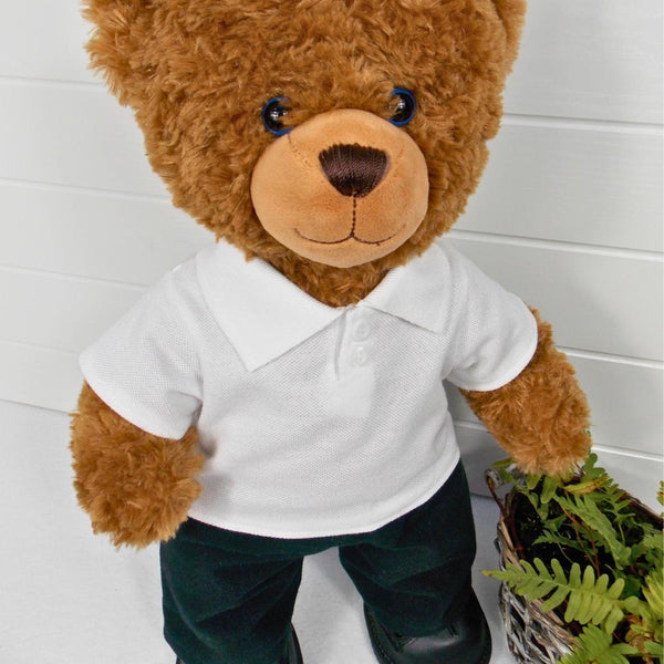 Brown teddy bear wearing a white polo t-shirt, black trousers / pants and black shoes. The teddy bear is standing in front of a white background with a green fern plant on the right. The teddy bear t-shirt and teddy bear pants have been made from sewing patterns by Best Dressed Bears.