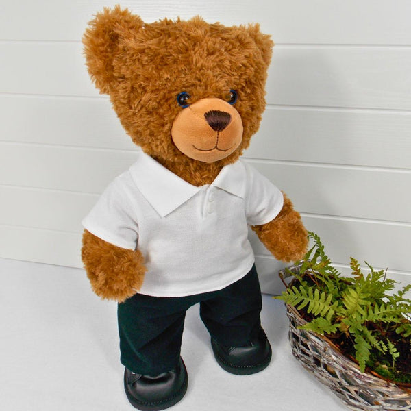 Brown teddy bear wearing a white polo t-shirt, black trousers / pants and black shoes. The teddy bear is standing in front of a white background with a green fern plant on the right. The teddy bear t-shirt and teddy bear pants have been made from sewing patterns by Best Dressed Bears.